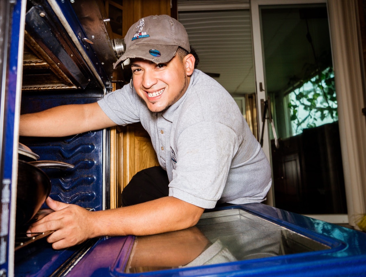 A smiling Doctor Maintenance technician working inside an oven on a Baltimore service call, the kind of real photo a Google Business Profile should carry instead of stock images