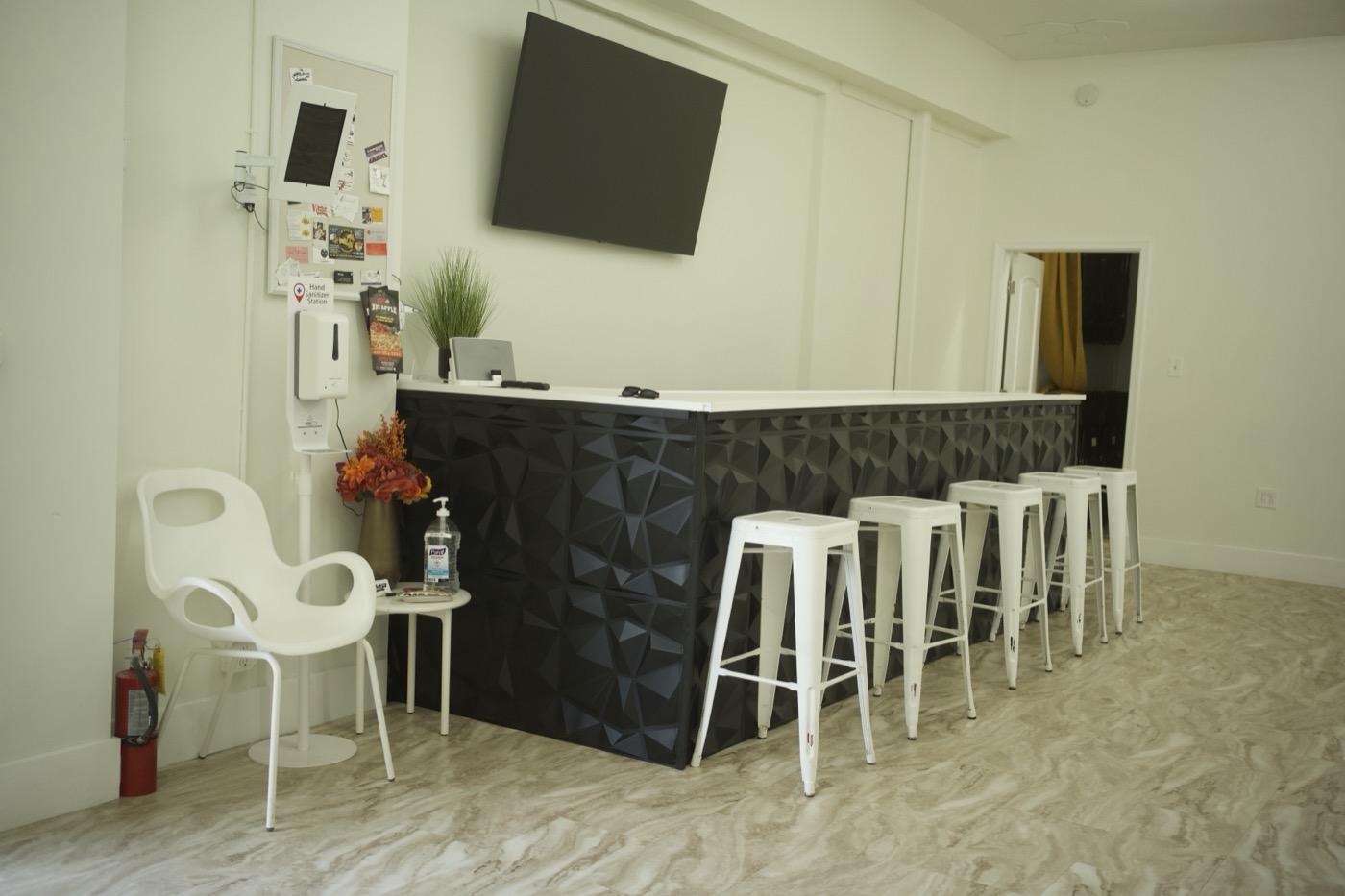 The bar area at Studio 87 with a black faceted-panel counter, a wall-mounted TV and white metal stools, one of the room amenities a wedding venue gallery is built to show off