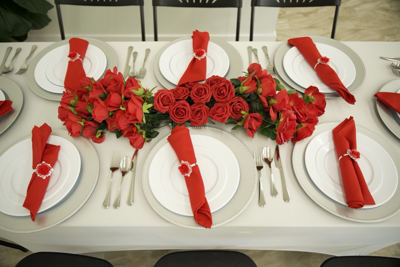 An overhead table styled with a red rose garland runner, red napkins in rose rings and silver chargers at Studio 87, the kind of real gallery photo a wedding inquiry converts on