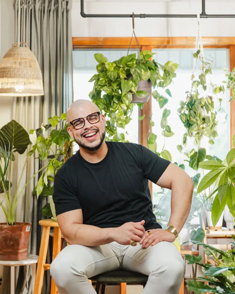 Willis Aybar, founder of Another Monday in Baltimore, MD, laughing on a stool in a plant filled room, the person owners talk to about Lovable alternatives before moving a website